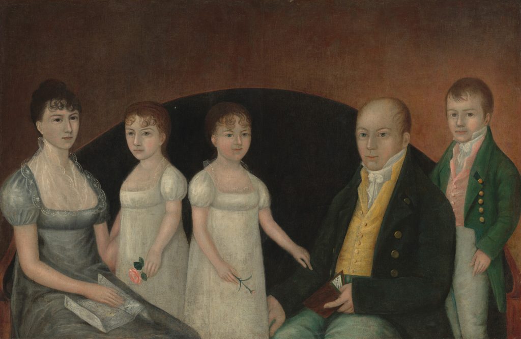 An early 19th-century family portrait showing five figures posed in front of a dark curved backdrop against a warm brown background. On the left, a seated woman in a gray dress with a lace collar holds an open book. Beside her stand two young girls in white dresses, each holding a flower. On the right, a seated man in a dark coat and yellow vest holds a small book or letter, while a young boy stands at the far right wearing a green jacket with brass buttons over a pink waistcoat. All figures face forward with calm, formal expressions in a folk-art style.