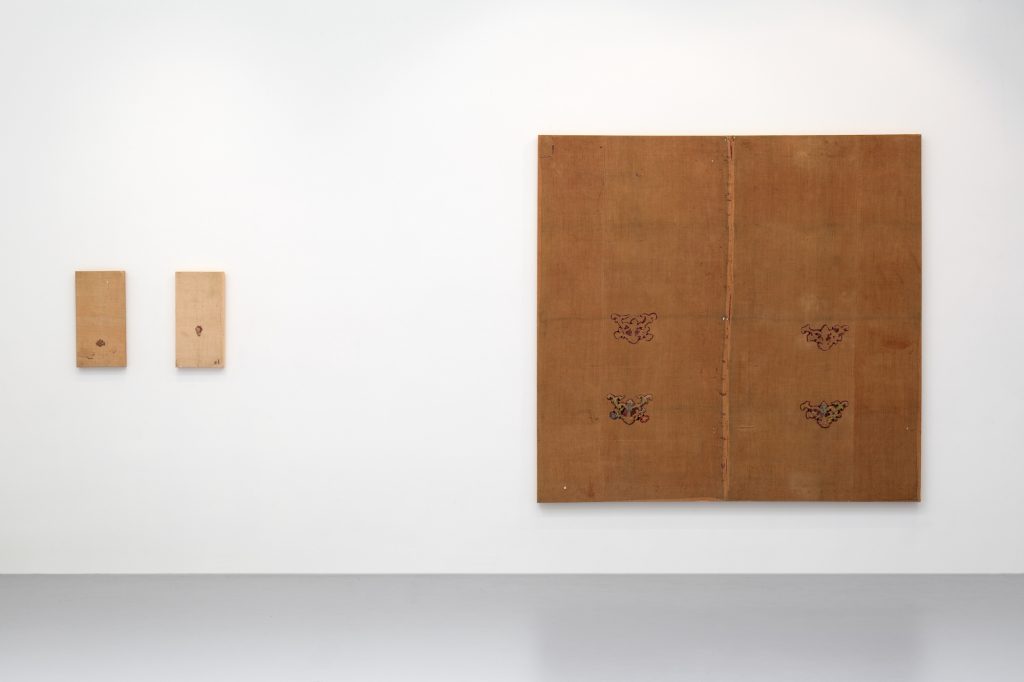 A white gallery space is pictured with brown paintings hanging on the wall