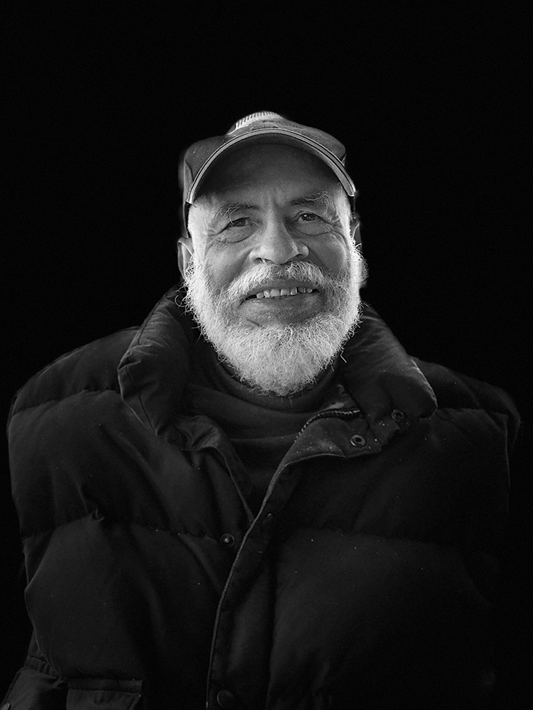 A black and white photo of Alonzo Davis as an elderly man. He is wearing a black coat and a black baseball hat, and has a thick white beard.