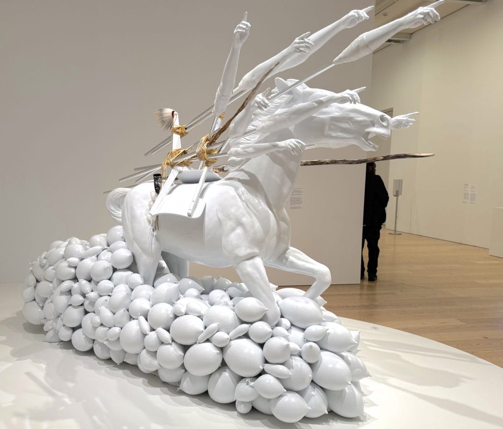A sculpture of a white horse being driven by a bodiless figure with arms outstretched toward the sky