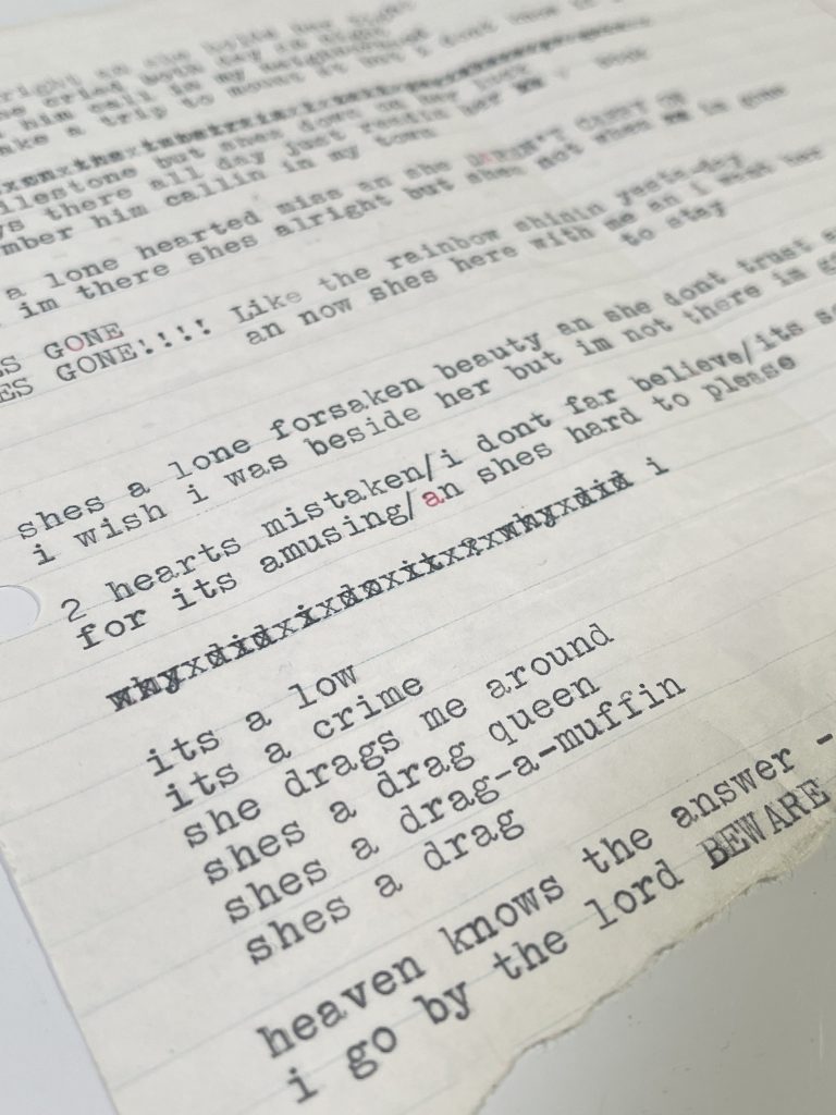 Close-up typed lyric sheet with corrections, crossed-out lines, and uneven text on lined paper
