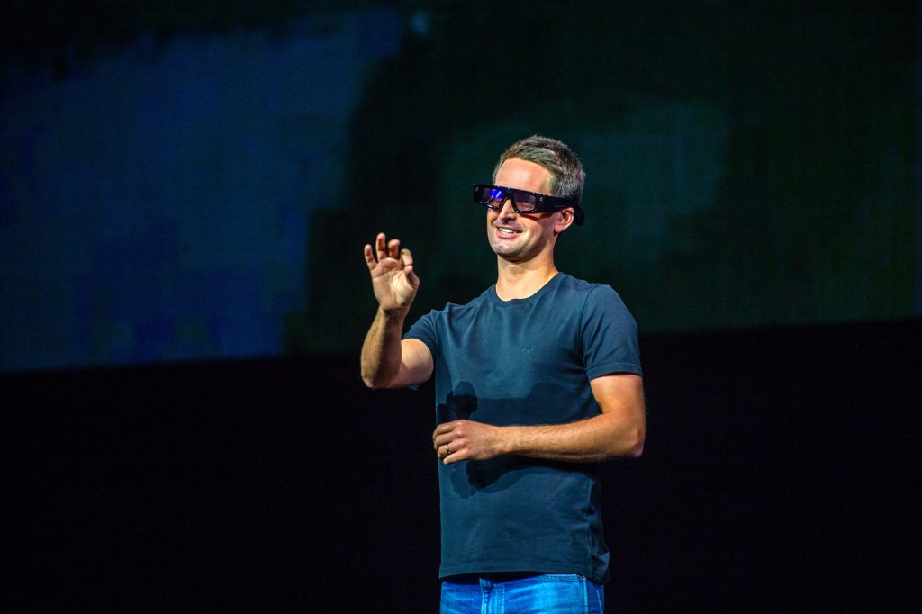 A man gesturing while wearing Snap's augmented reality glasses on a stage