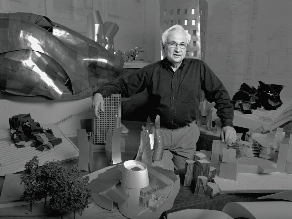 A black and white photograph of an older white man standing in front of curvilinear forms