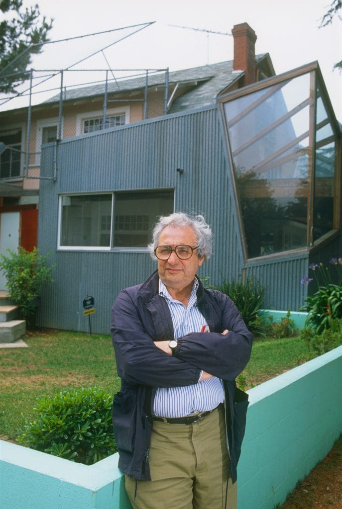 Architect standing outside a modern, deconstructivist-style house featuring corrugated metal and angular glass additions.