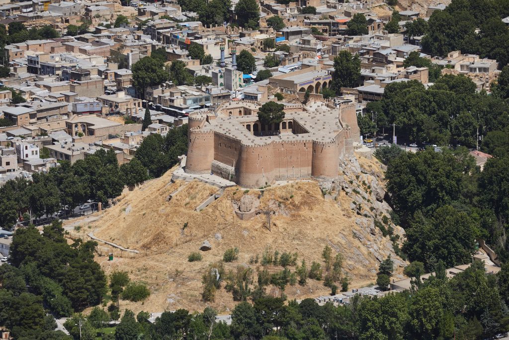 Aerial view of historic brick fortress atop hill surrounded by dense urban neighborhood and trees.