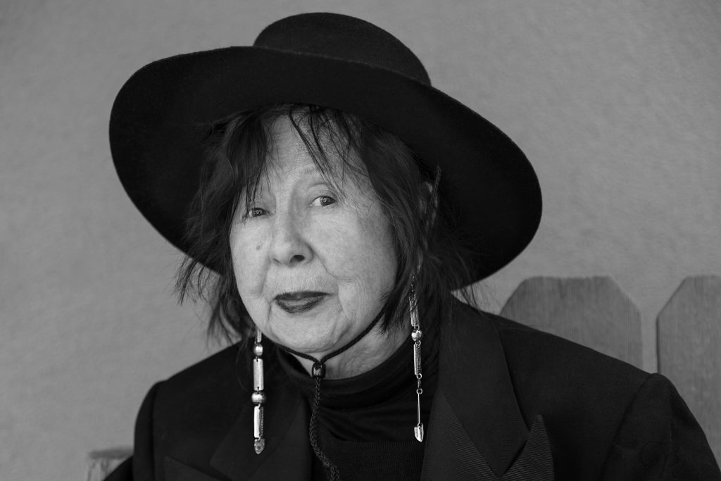 Black and white photograph of Jaune Quick-to-See Smith wearing a black hat and long earrings