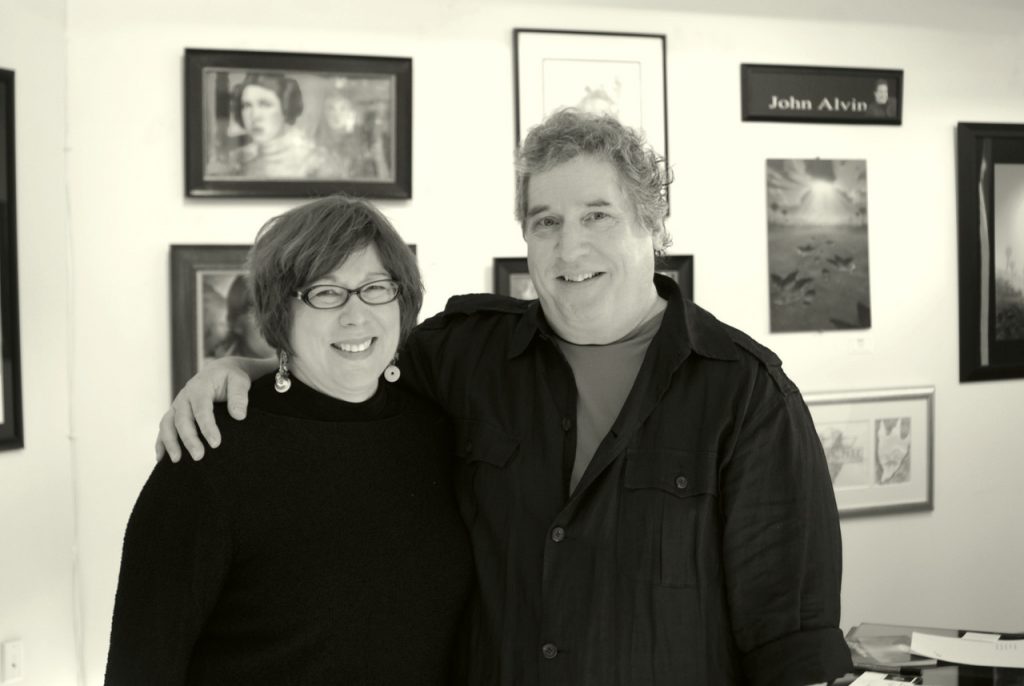 John Alvin and Andrea Alvin smile together at gallery exhibition, surrounded by framed film poster artworks.