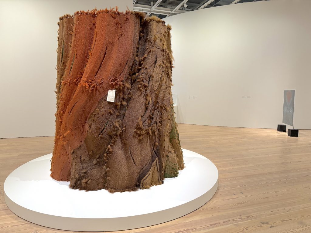 A monumental, eight-foot-tall sculpture resembling a massive tree trunk