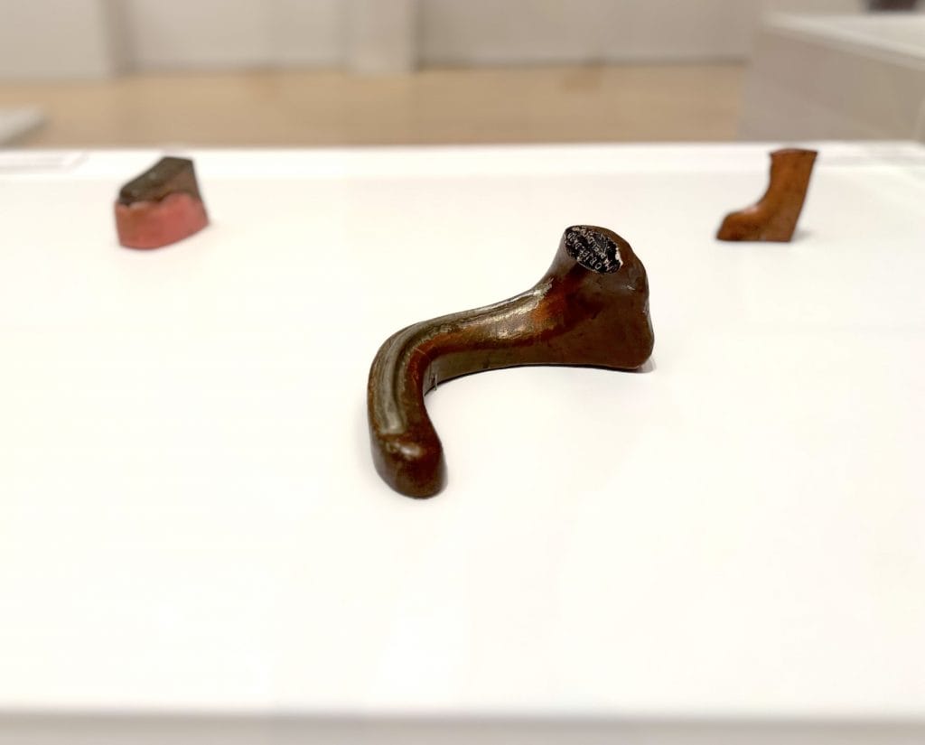 Three small, biomorphic bronze sculptures by Marcel Duchamp, including Objet-dard, resting on a white museum plinth with a blurred gallery background.