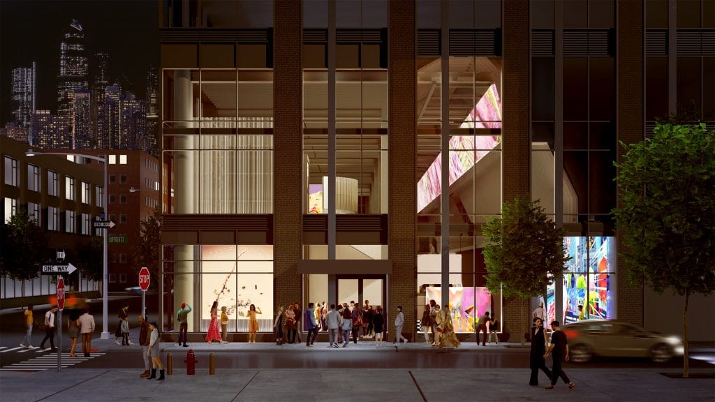 Nighttime view of glass-fronted building glowing with color, pedestrians gathered outside in urban setting.