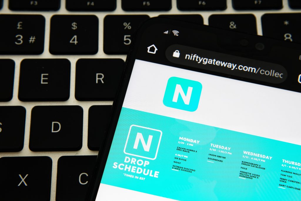 Smartphone displaying Nifty Gateway drop schedule webpage resting on laptop keyboard, highlighting NFT marketplace branding.