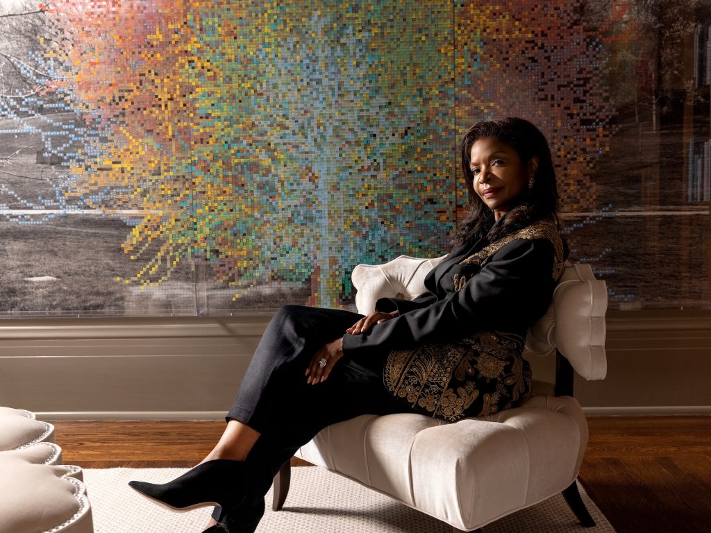 A Black woman, Pamela Joyner, relaxes in front of an artwork
