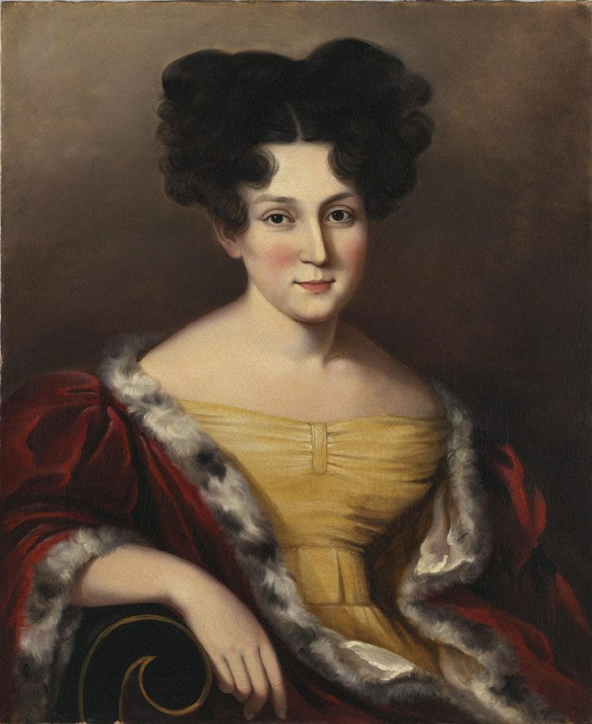 A Sarah Miriam Peale portrait painting of a young white woman with pale skin and dark brown hair styled in large, voluminous curls parted at the center, wearing an off-the-shoulder golden dress and a red velvet shawl trimmed with fur, seated with one arm resting on a curved armrest against a dark, neutral background, her expression calm and composed with soft pink cheeks and direct gaze