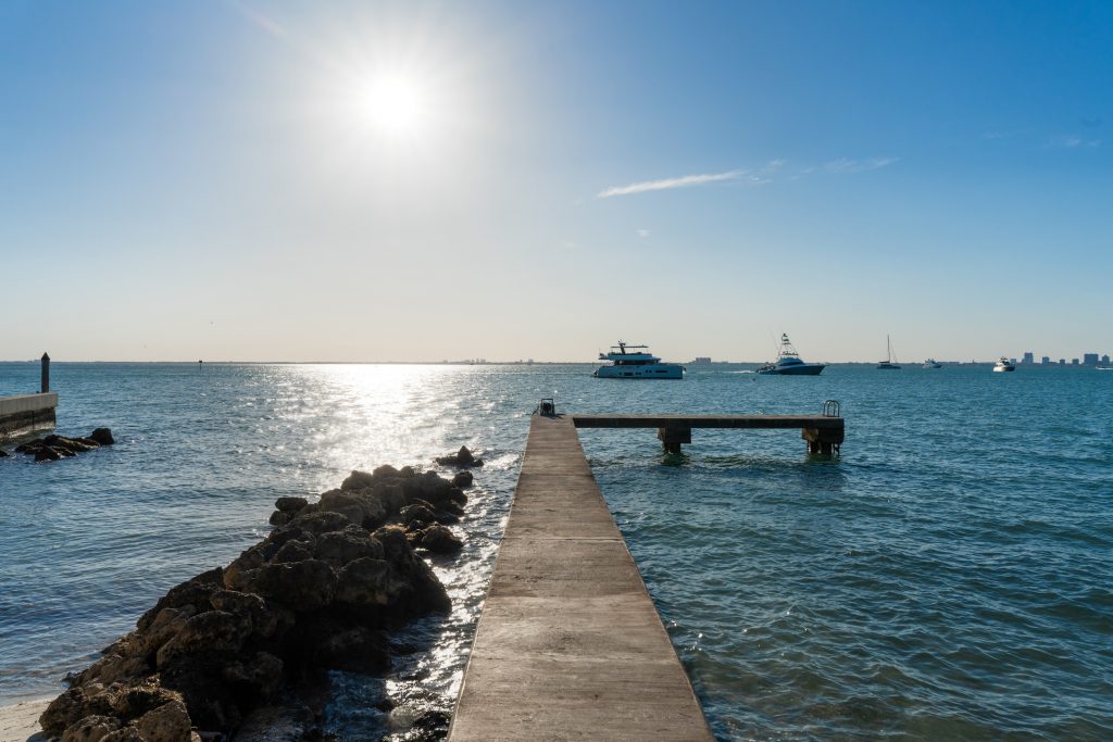 A small dock extends into Biscayne Bay in Florida, with boats on the water in the distance