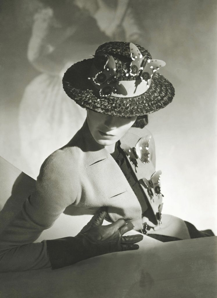 Woman in structured jacket and wide-brim hat adorned with butterflies, posing dramatically in studio light