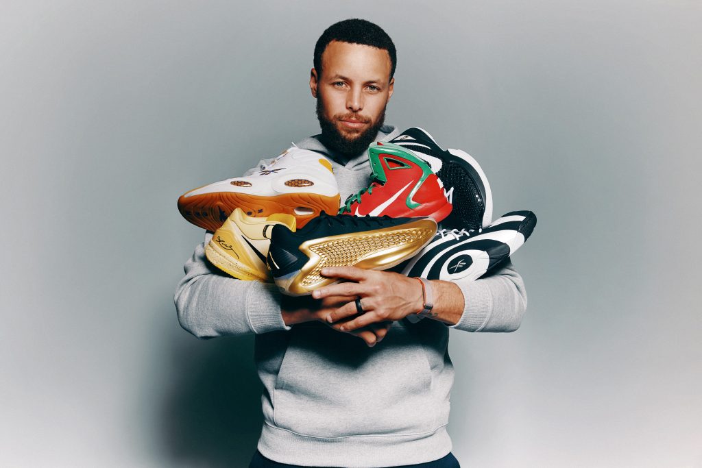 Athlete holding multiple colorful basketball sneakers, studio portrait highlighting shoes against neutral background